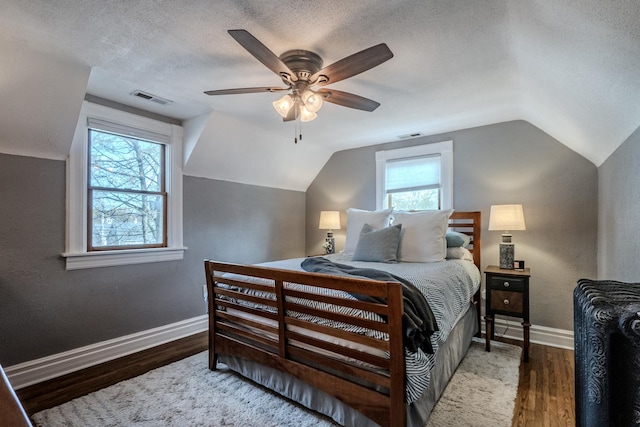 bedroom with vaulted ceiling, a textured ceiling, baseboards, and wood finished floors