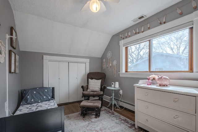 sitting room with baseboard heating, vaulted ceiling, a ceiling fan, wood finished floors, and visible vents