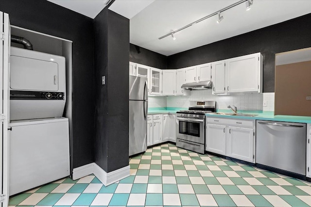kitchen with light floors, stacked washer and dryer, under cabinet range hood, a sink, and stainless steel appliances