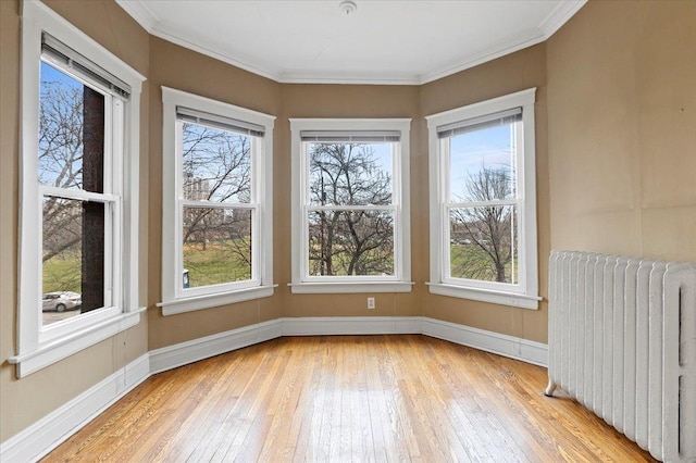 spare room with crown molding, light wood-style flooring, radiator, and baseboards