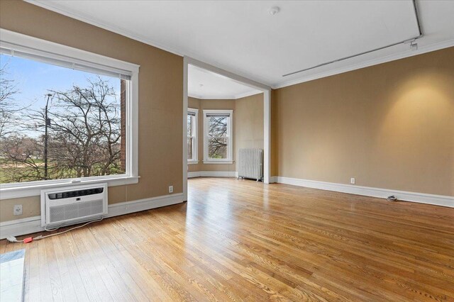 unfurnished living room featuring crown molding, a wall unit AC, radiator heating unit, light wood finished floors, and baseboards
