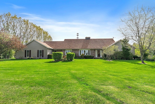 ranch-style home featuring brick siding, a chimney, and a front yard