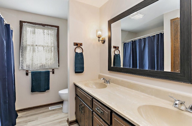 full bathroom featuring a sink, double vanity, toilet, and wood finished floors