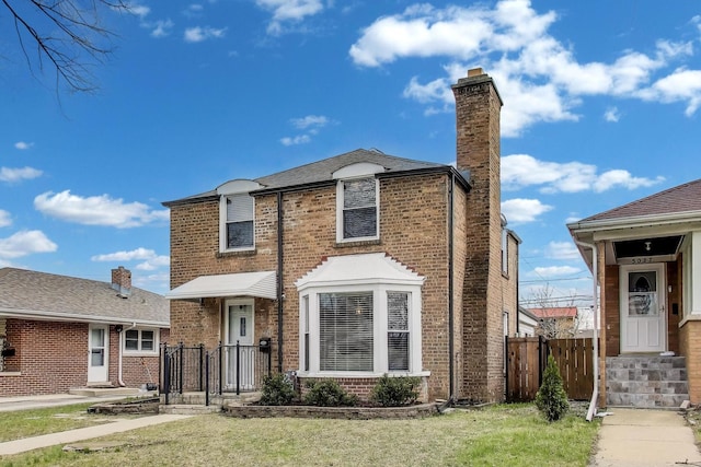 view of front facade with a chimney, a front lawn, brick siding, and fence