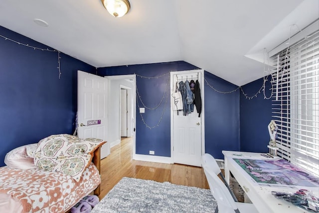 bedroom with vaulted ceiling, wood finished floors, and baseboards