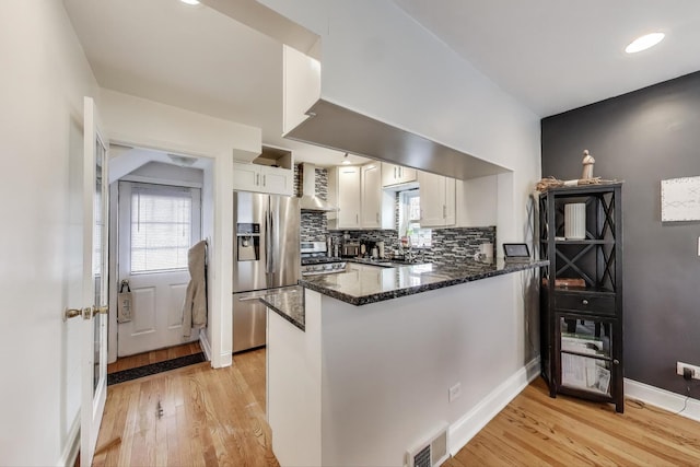 kitchen with stainless steel appliances, light wood-style floors, dark stone counters, a peninsula, and white cabinetry