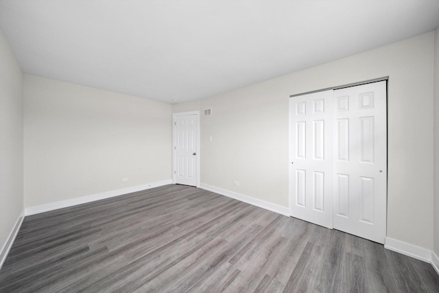 unfurnished bedroom featuring baseboards, wood finished floors, and a closet