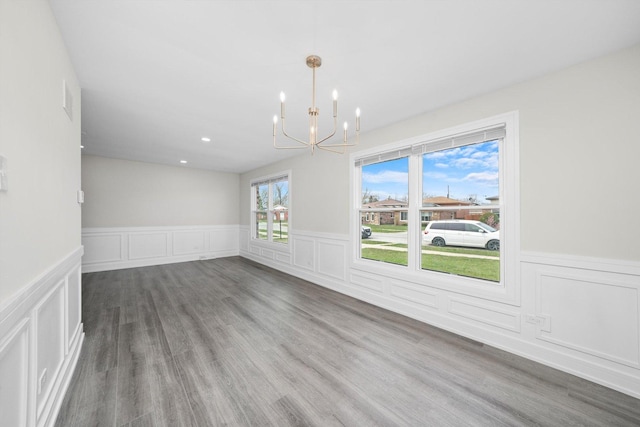 unfurnished dining area featuring wainscoting, a decorative wall, a notable chandelier, and wood finished floors