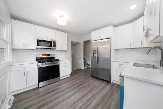 kitchen with white cabinets, stainless steel appliances, a sink, decorative backsplash, and wood finished floors