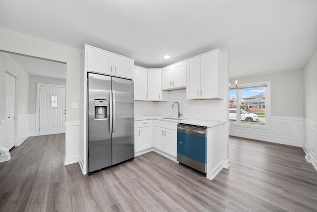 kitchen with wood finished floors, a sink, stainless steel fridge, light countertops, and dishwashing machine