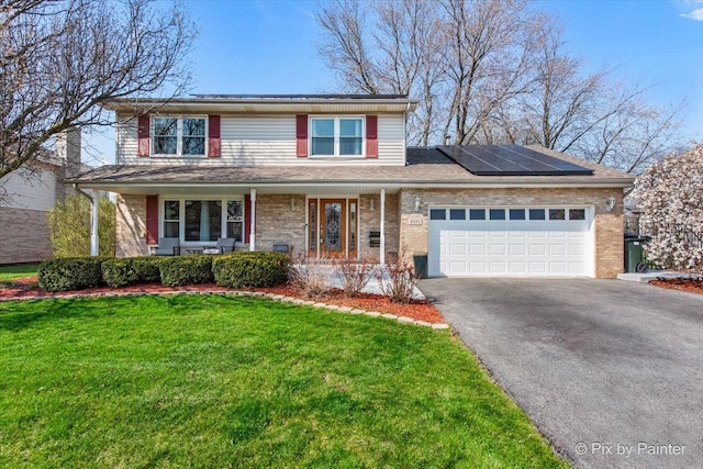 traditional home with roof mounted solar panels, an attached garage, a porch, a front lawn, and driveway