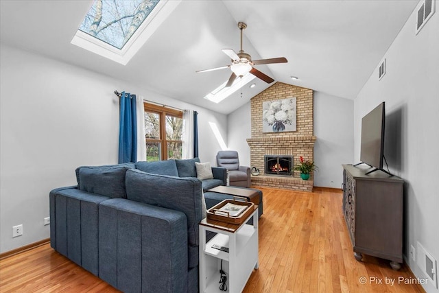 living area featuring visible vents, vaulted ceiling with skylight, a ceiling fan, light wood-style floors, and a fireplace