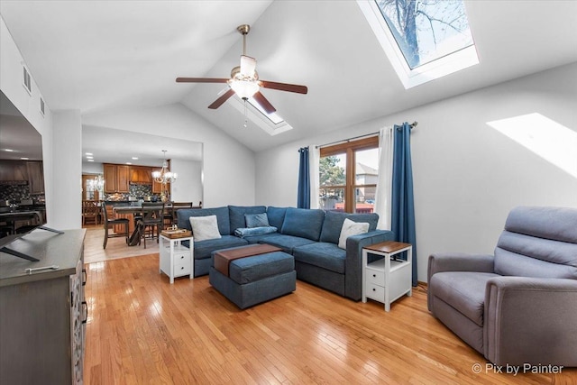 living area featuring vaulted ceiling with skylight, visible vents, ceiling fan with notable chandelier, and light wood finished floors