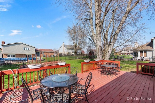 wooden terrace with outdoor dining space, a residential view, a fenced backyard, and a lawn