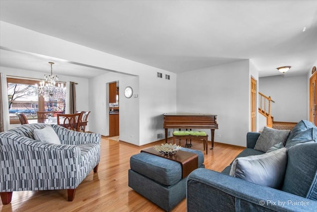 living area with an inviting chandelier, light wood-style flooring, visible vents, stairs, and baseboards