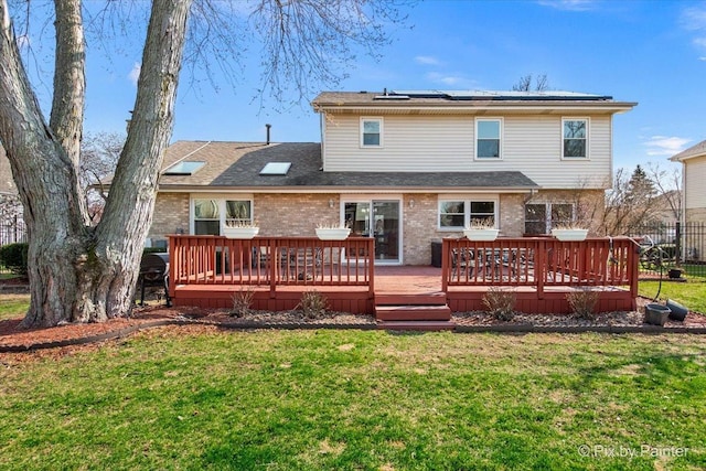 rear view of property with roof with shingles, brick siding, a wooden deck, a yard, and roof mounted solar panels