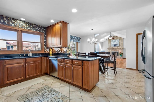 kitchen featuring light tile patterned floors, brown cabinetry, appliances with stainless steel finishes, a sink, and dark countertops