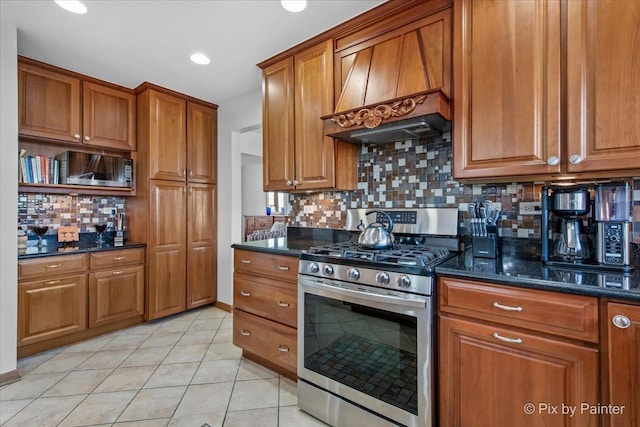 kitchen with custom exhaust hood, gas stove, light tile patterned flooring, brown cabinets, and decorative backsplash