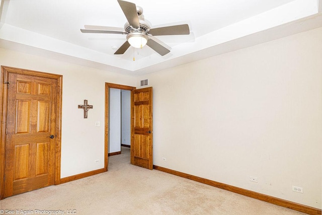 empty room featuring visible vents, light carpet, baseboards, a tray ceiling, and a ceiling fan