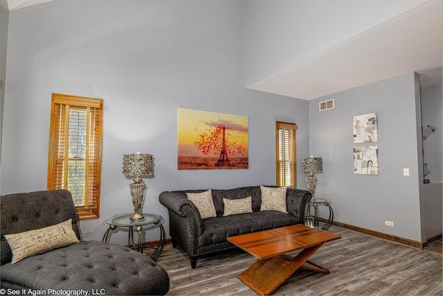living area with baseboards, visible vents, wood finished floors, and a towering ceiling