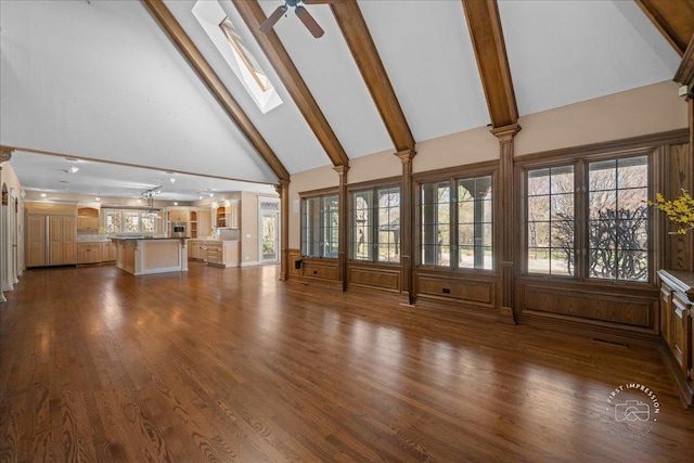 unfurnished living room featuring high vaulted ceiling, a ceiling fan, a skylight, beamed ceiling, and dark wood-style flooring