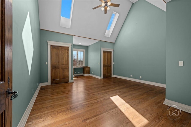 interior space featuring baseboards, wood finished floors, a skylight, and high vaulted ceiling