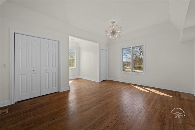unfurnished bedroom with wood finished floors, baseboards, two closets, and an inviting chandelier