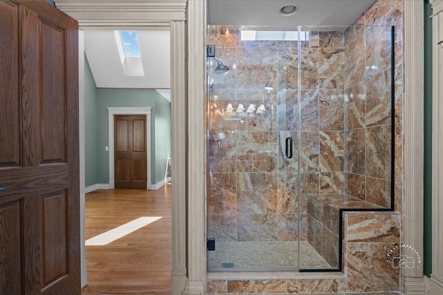 bathroom featuring a skylight, baseboards, wood finished floors, and a shower stall