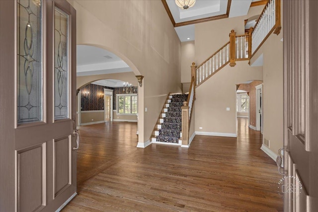 foyer featuring stairway, a towering ceiling, wood finished floors, arched walkways, and baseboards