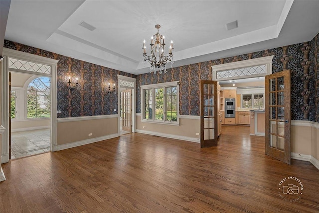 unfurnished dining area with wallpapered walls, wood finished floors, a notable chandelier, and a raised ceiling