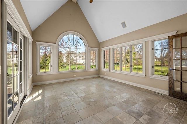 unfurnished sunroom with stone tile floors, baseboards, visible vents, and high vaulted ceiling