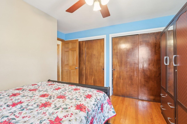 bedroom featuring light wood-style flooring, ceiling fan, and multiple closets