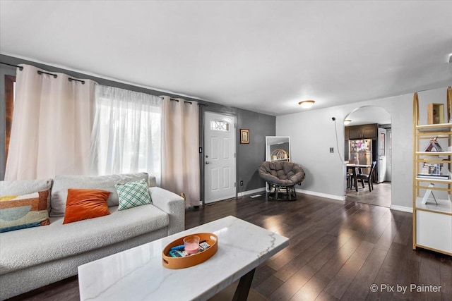 living area with arched walkways, baseboards, and dark wood-style flooring