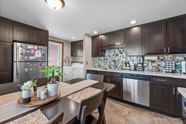 kitchen featuring stainless steel appliances, a sink, washing machine and dryer, dark brown cabinetry, and tasteful backsplash
