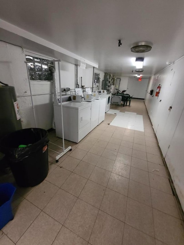 clothes washing area with water heater, washing machine and clothes dryer, and light tile patterned flooring