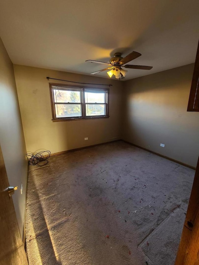 carpeted spare room featuring baseboards and a ceiling fan