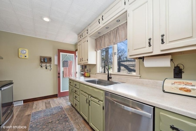 kitchen with wood finished floors, dishwasher, light countertops, a sink, and green cabinetry
