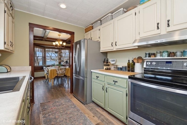 kitchen with an inviting chandelier, green cabinetry, appliances with stainless steel finishes, under cabinet range hood, and light wood-style flooring