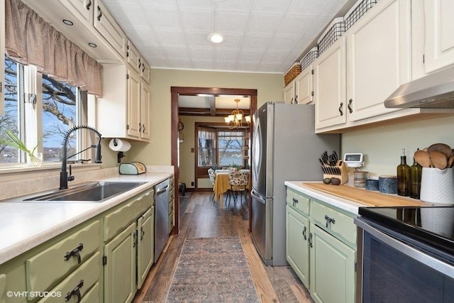 kitchen with green cabinets, a chandelier, light countertops, a sink, and stainless steel appliances