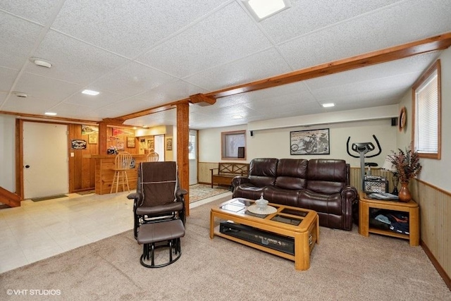 living area featuring wood walls, a wainscoted wall, a drop ceiling, and carpet floors