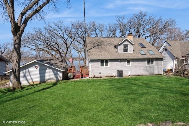 rear view of house with central AC unit, roof with shingles, a lawn, and a chimney