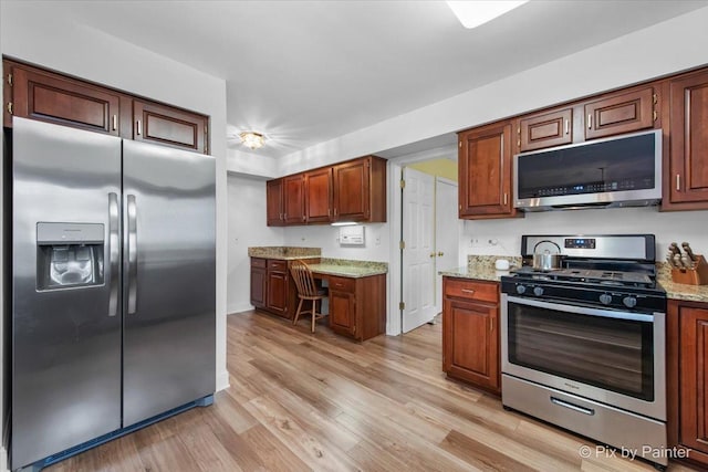 kitchen with light wood-type flooring, light stone counters, and appliances with stainless steel finishes