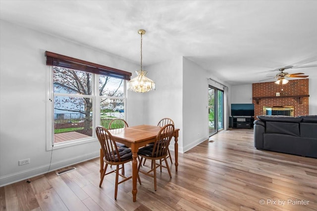 dining space with ceiling fan with notable chandelier, baseboards, light wood-type flooring, and visible vents