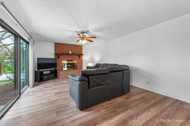 living room featuring light wood-type flooring, a brick fireplace, a ceiling fan, and baseboards
