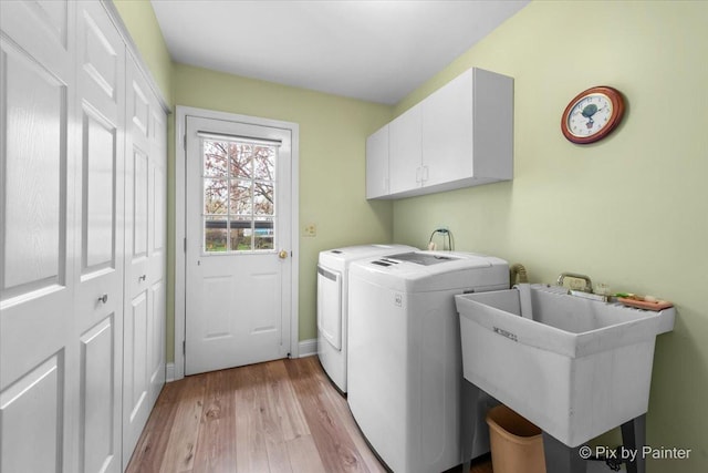 laundry area featuring washing machine and clothes dryer, a sink, cabinet space, light wood-style flooring, and baseboards