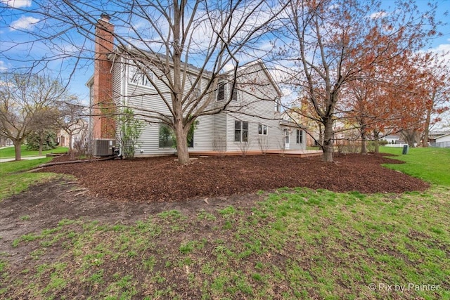 view of side of home featuring a chimney, a yard, and central AC unit