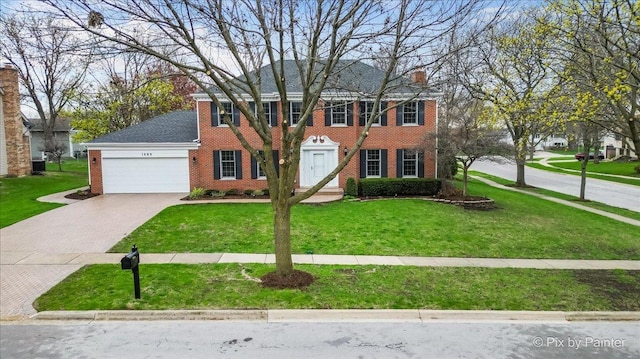 colonial inspired home featuring a front lawn, driveway, a chimney, brick siding, and a garage