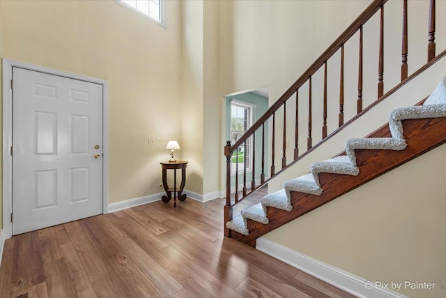 foyer featuring stairway, baseboards, wood finished floors, and a towering ceiling