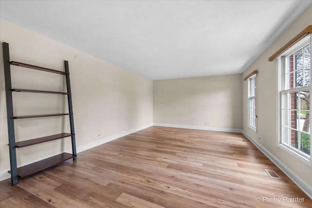 empty room featuring plenty of natural light, visible vents, and light wood-type flooring
