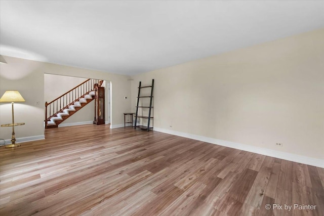 unfurnished living room featuring baseboards, wood finished floors, and stairs